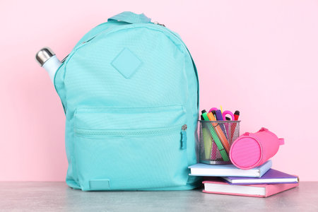 Backpack with different school stationery on light gray table against pink backgroundの写真素材