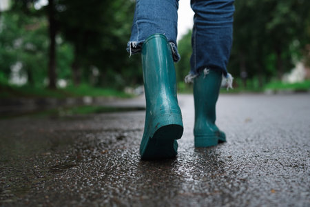 Woman in turquoise rubber boots walking on wet road, closeup. Space for textの写真素材
