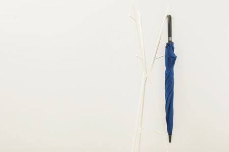Blue umbrella on clothing rack against white background, space for textの写真素材
