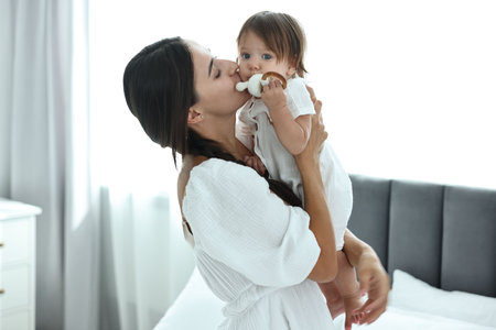 Beautiful young mother and her cute little baby with rattle in bedroomの写真素材