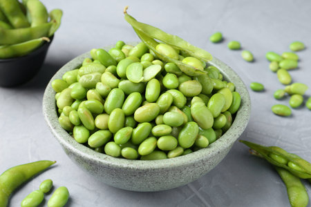 Fresh edamame soybeans in bowl and pods on gray textured table, closeupの写真素材