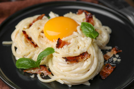 Delicious pasta Carbonara with egg yolk, bacon and basil on plate, closeupの写真素材
