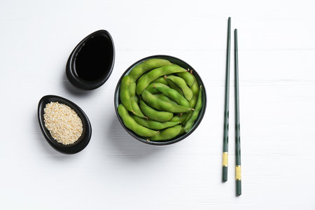 Fresh edamame pods, soy sauce and seeds on white wooden table, flat layの写真素材