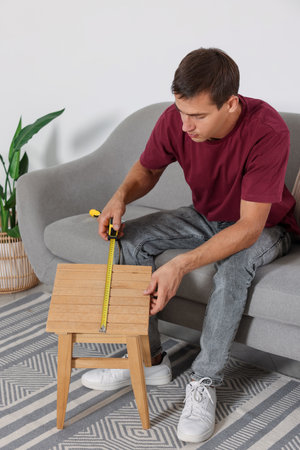 Man using tape measure while repairing wooden stool indoorsの写真素材