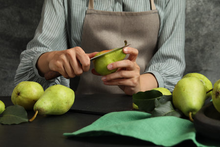 Woman cutting fresh ripe pear at black table, closeupの写真素材