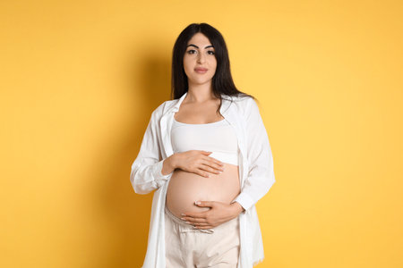 Portrait of beautiful pregnant woman on yellow backgroundの写真素材
