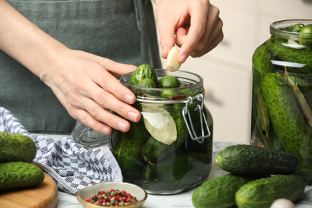 Making pickles. Woman putting garlic into glass jar at table, closeupの写真素材