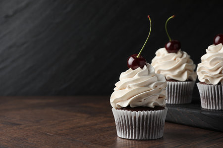 Delicious cupcakes with cream and cherries on wooden table, space for textの写真素材