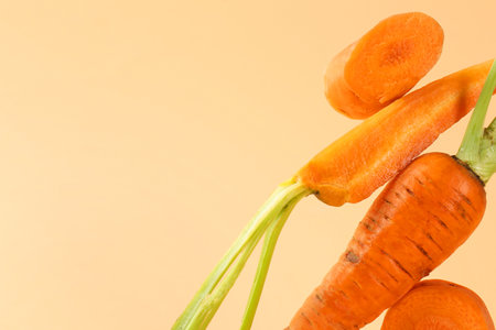 Whole and cut fresh carrots on pale orange background, closeup. Space for textの写真素材