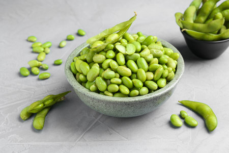 Fresh edamame soybeans in bowl and pods on gray textured table, closeupの写真素材