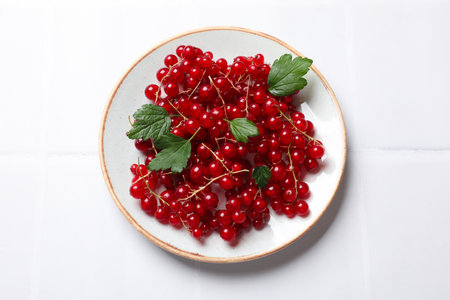 Fresh red currents and green leaves on white table, top view