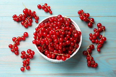 Fresh red currents in bowl on light blue wooden table, top view