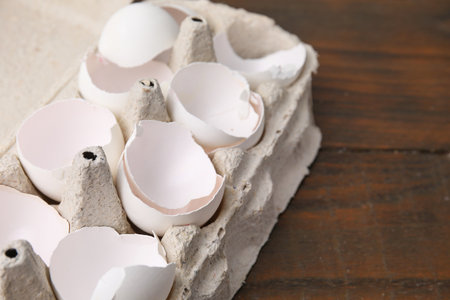 Broken eggshells in carton on wooden table, closeup. Space for text