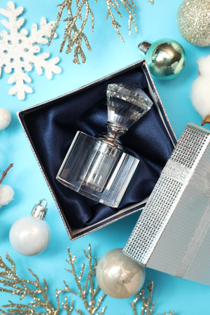 Perfume bottle in gift box and Christmas decor on light blue background, flat lay