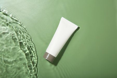Tube with cream in water on light green background, top view. Cosmetic productの写真素材