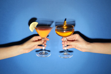 Friends with glasses of refreshing cocktails on blue background, closeup