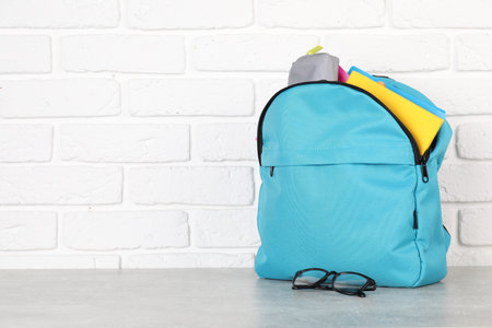 Backpack with different school stationery on light gray table near brick wall. Space for textの写真素材