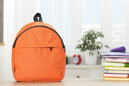 Backpack with different school stationery on desk in room. Space for text