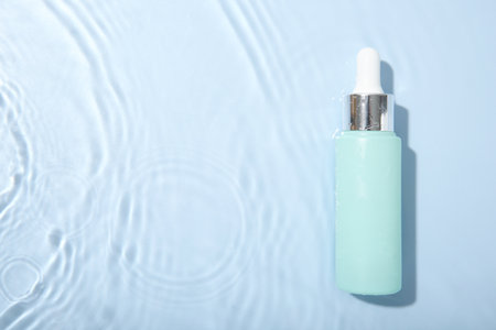 Bottle of cosmetic product in water on light blue background, top view. Space for textの写真素材