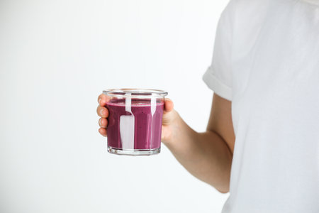 Woman with glass of tasty fresh acai juice on light gray background, closeup