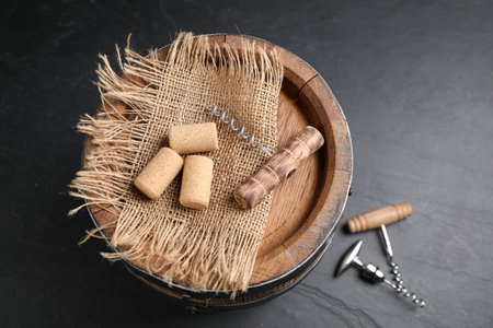 Different corkscrews, corks and wooden barrel on gray table, above view