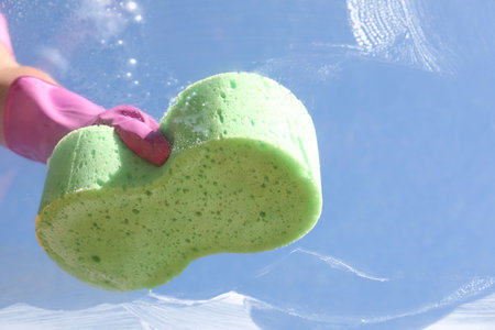 Woman washing window with sponge against blue sky, closeupの写真素材