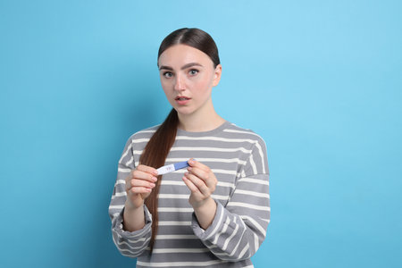 Shocked woman holding pregnancy test on light blue backgroundの写真素材