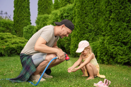 Father with hose spraying water and his daughter on lawn in backyardの写真素材