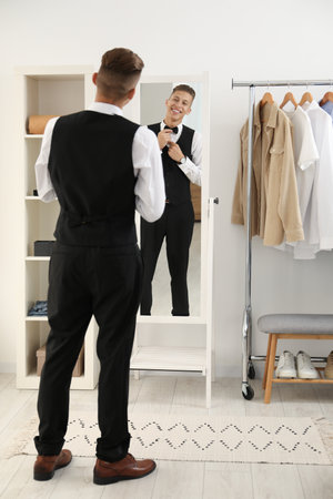 Handsome man adjusting bow tie near mirror indoorsの写真素材