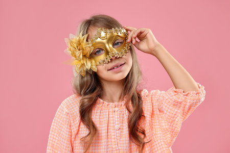 Cute girl wearing carnival mask on pink backgroundの写真素材