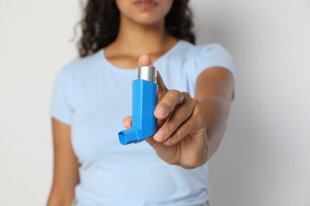 Woman holding asthma inhaler on light gray background, closeup
