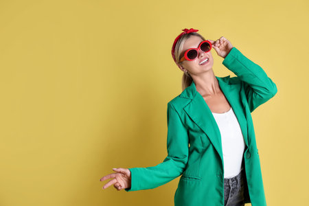 Beautiful woman in stylish green jacket on yellow background, space for textの写真素材