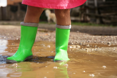 Little girl wearing green rubber boots standing in puddle outdoors, closeupの写真素材