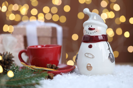 Funny snowman figure, cup, dried orange slices and cinnamon on artificial snow against blurred lightsの写真素材