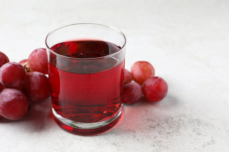 Tasty grape juice in glass and berries on light textured table, closeup. Space for textの写真素材