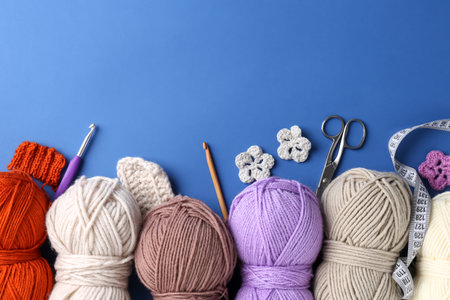 Different colorful yarns, crochet flowers, hooks and scissors on blue background, flat lay. Space for textの写真素材