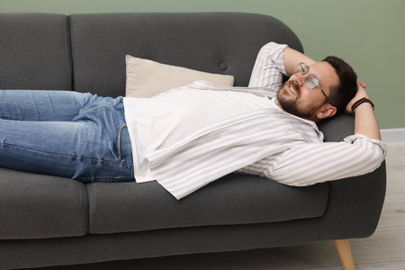 Smiling man with hands behind his head relaxing on sofa at homeの写真素材