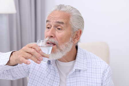 Handsome man senior drinking water at homeの写真素材