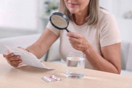 Senior woman with magnifying glass reading medicine instruction at table indoors, closeupの写真素材