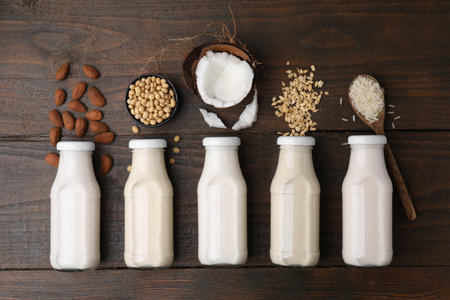 Different types of vegan milk in bottles and ingredients on wooden table, flat layの写真素材