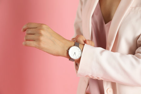 Beautiful woman in stylish white suit and watch on pink background, closeupの写真素材