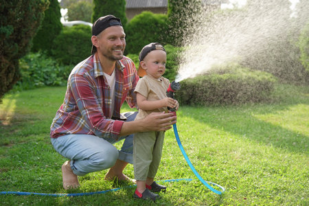 A person and child watering lawn with hose in backyardの写真素材