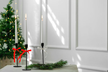 Burning candles on white table and Christmas tree at home, space for text