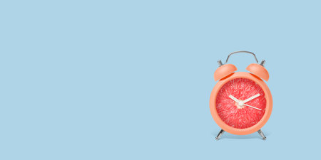Juicy grapefruit on alarm clock dial against light blue background. Creative poster with space for text, banner designの写真素材