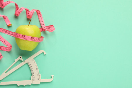 Body fat caliper, measuring tape and apple on turquoise background, flat lay. Space for textの写真素材