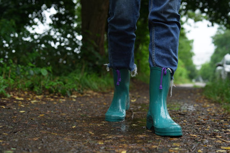 Woman in turquoise rubber boots walking on wet road, closeup. Space for textの写真素材