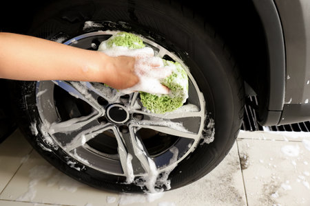 Man washing car wheel with sponge indoors, closeupの写真素材