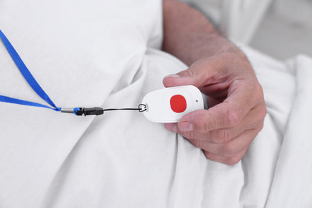 Senior man with emergency call button on bed in hospital, closeup