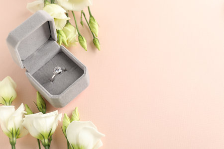 Beautiful ring with gemstone in box and flowers on pink background. Space for text