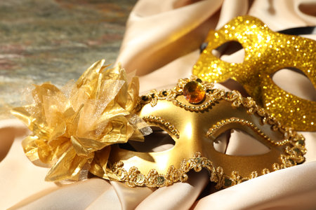 Beautiful golden carnival masks and beige fabric on table, closeupの写真素材